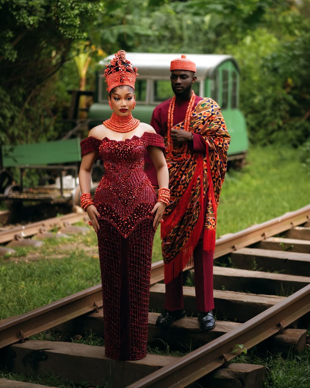 A noiva em vestido vinho bordado com coral e o noivo com pano kente
